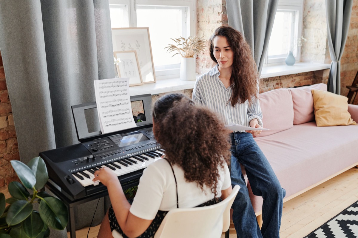 A music teacher beside a student at a keyboard