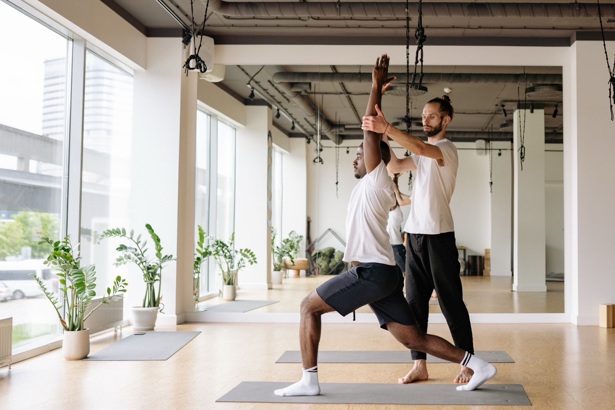 A yoga teacher adjusting a student's pose in a bright studio